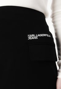 Juoda sijonas iš Karl Lagerfeld Jeans, su kišene ir išsiuvinėtu logotipu. Lygi medžiaga su prigludusia forma.