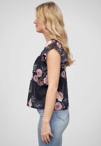 Blouse florale bleu marine avec des manches courtes à volants, ornée de fleurs roses et blanches, fabriquée en tissu léger, avec une coupe décontractée et un ourlet arrondi.
