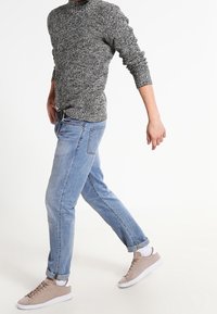 Grijze gebreide trui met textuur, lichtblauwe spijkerbroek en beige sneakers met witte zolen. Casual outfit met een ontspannen pasvorm en opgerolde mouwen.