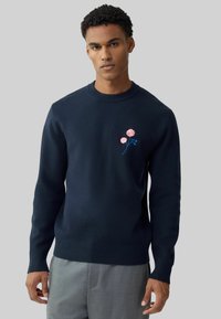 Pulover bleumarin realizat din material moale, cu manșete și tiv reiate, decorat cu broderie de floare roz pe partea stângă a pieptului.