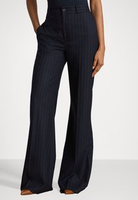 Pantaloni a righe navy con vita aderente, gambe larghe e tasche laterali; presenta una chiusura con bottone e una trama di tessuto liscia.