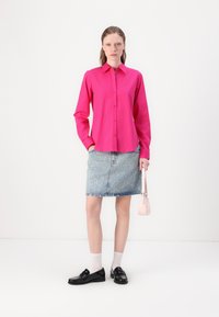 Fuchsia button-up shirt, light blue denim skirt with “Hugs” print, black loafers, white ankle socks, and small pink handbag.
