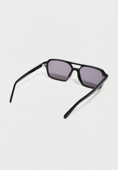 Μαύρα ορθογώνια γυαλιά ηλίου με φακούς με μοβ απόχρωση και διπλή γέφυρα, ανοιχτά τοποθετημένα σε λευκή επιφάνεια.