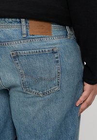 Jeans in denim azzurro chiaro con gamba dritta, dotati di tasche posteriori e una patch in pelle marrone con il logo sulla vita.