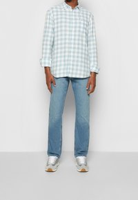 Ljusblå och vit rutigt skjorta med knäppning och långa ärmar, kombinerad med ljusblå jeans och grå sneakers med vita snören och bruna detaljer.