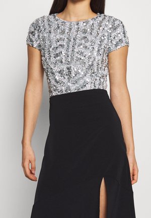 Vrouw die een zilveren, met pailletten versierde top met korte mouwen draagt, gecombineerd met een hoge taille zwarte rok met een vooraan gesplitste zoom.