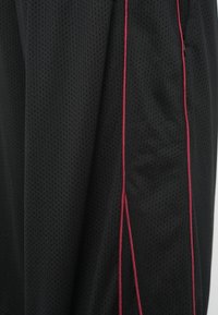 Μαύρα αθλητικά σορτς από διαπνέον ύφασμα με δίχτυ, με κόκκινες ρίγες περιμετρικά στα πλαϊνά ραφές και υφή με ανάγλυφο φινίρισμα.