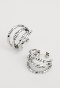 Silver hoop earrings featuring three spiraled bands, polished metal finish, and a stud back closure. Smooth texture with shiny surface.