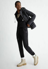 Giubbotto puffa nero sopra una maglia nera con un design grafico, abbinato a pantaloni jogger neri e stivaletti beige con suola chunky.
