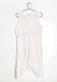 Valkoinen, hihaton mekko, jossa on röyhelöhelma, tekstiiliset sivupaneelit ja pehmeä, kevyt kangas. Ripustettuna mustalle koukulle.