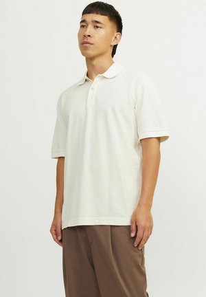 Polo skjorte i lys creme, kortærmet, lavet af blødt stof, har en tre-knaps lukning og diskret logo broderi på brystet.