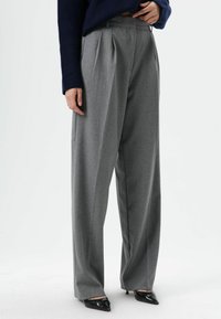 Gray high-waisted trousers with pleats, made of a textured fabric. Features wide legs and are paired with pointed black heels.