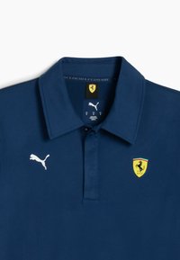 Jūrinio stiliaus polo marškiniai su apykakle, turintys baltą Puma logotipą ir Ferrari emblema su geltonu fonu bei šokančio žirgo dizainu.