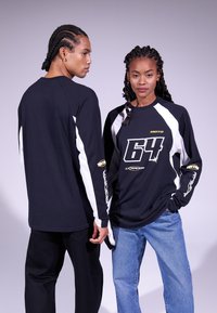 Black long-sleeve shirts with white accents, featuring graphic number "64" in yellow. Worn with dark pants and light blue jeans.