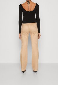 Top nero a maniche lunghe con una scollatura larga sulla schiena. Pantaloni beige con una texture liscia, zip frontale e cuciture laterali in evidenza.