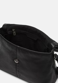 Zwarte leren handtas met een gladde textuur, magnetische sluiting en een ritsvak aan de binnenkant. Het interieur is gevoerd met stof.