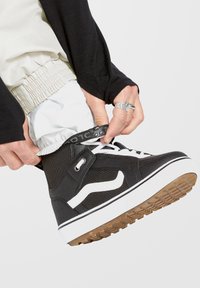 Baskets montantes noires en toile avec des accents blancs, semelle en caoutchouc et dessus texturé. Présente un design à lacets et une sangle de cheville réglable.