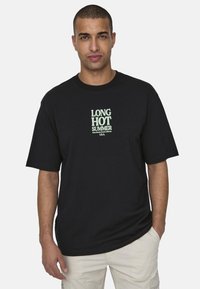 Czarna bawełniana koszulka z zielonym napisem "DŁUGIE GORĄCE LATO" oraz szczegółami "Santa Monica Beach Kalifornia" poniżej. Krótkie rękawy, dekolt w serek.