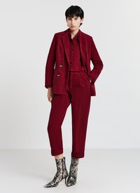 Karmesinroter Kordanzug mit zweireihigem Sakko, hoch taillierter Hose und aufgerollten Bündchen. Kombiniert mit spitzen Stiefeletten im Schlangenlederdruck.