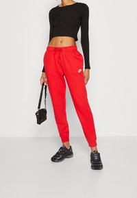 Červené tepláky s elastickým pasem a šňůrkou, s malým bílým logem Nike. V kombinaci s černým krátkým rukávem a černými teniskami.