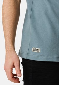 Ljusblå bomulls t-shirt med korta ärmar, med en lapp vid fållen och i kombination med svarta byxor. Subtil textur, avslappnad passform.