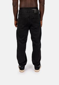 Czarne dżinsy o luźnym kroju, z dwoma tylnymi kieszeniami i płaskim, elastycznym paskiem. Noszone z czarnymi trampkami.