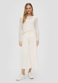 Top bianco trasparente a maniche lunghe con texture a righe orizzontali, abbinato a pantaloni a vita alta beige a gamba larga e sneakers bianche.