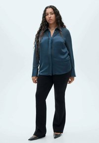 Teal satin blouse with a button-down front and long sleeves, paired with black trousers, and pointed black shoes with studded accents.