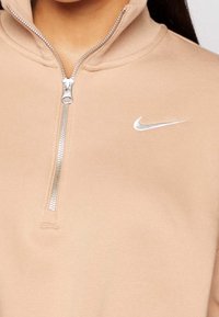 Light beige quarter-zip sweatshirt made of soft fabric. Features a silver zipper and a small silver Nike logo on the left chest.