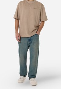 Béžové oversized tričko s krátkými rukávy a kulatým výstřihem, doplněné o světle modré džíny s volným střihem a bílé tenisky.