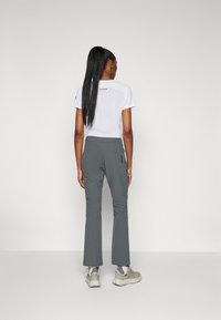 Hvit idrettsgenser med korte ermer og logo på baksiden, parret med grå tights med stretch, som har sidelommer og rett ben-design.