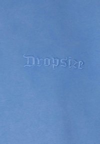 Lys blå stof med en glat tekstur, der har ordet "Dropsize" prægede i en dekorativ skrifttype.