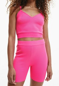 Rosa ribbad crop top med justerbara axelband, kombinerad med matchande högmidjade cykelshorts. Båda har en mjuk, stretchig textur.