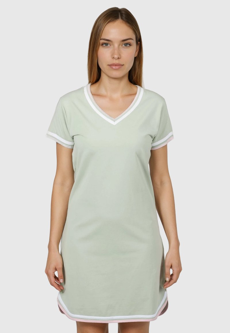 Donna che indossa un vestito verde chiaro a maniche corte con scollo a V e bordo bianco, in piedi davanti a uno sfondo semplice.