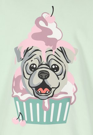 Un tissu vert menthe présente un chien en cartoon avec un design de cupcake, surmonté de glaçage rose et d'une cerise. Les yeux du chien sont grands, et les détails sont rehaussés de noir.