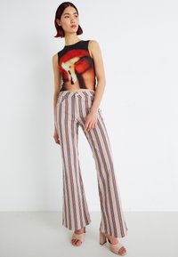 Haut sans manches avec un design en flammes ; associé à un pantalon taille haute à jambes larges arborant des rayures verticales rouges, bleues et crème.