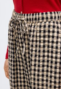 Κοντινό πλάνο μιας ασπρόμαυρης καρό φούστας με φιόγκο στη μέση, φορεμένη με κόκκινο ριμπ τοπ και εμφανές χέρι στο πλάι.