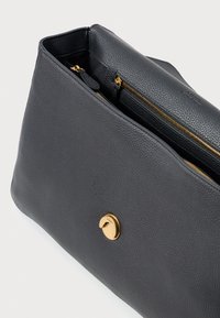 Bolsa de couro preta com textura pebble, apresentando um fecho em tom dourado e compartimentos com zíper duplo para armazenamento organizado.