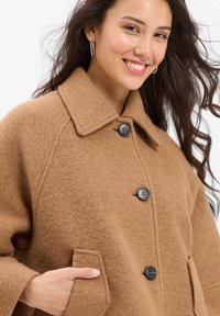 Brown wool blend coat with a collar, three black buttons, and patch pockets. Textured fabric and relaxed fit.