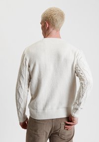 Maglione a treccia color crema con corpo testurizzato e maniche lavorate a maglia, rifinito con polsini e orlo a coste.