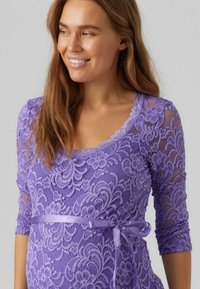 Krajkový tehotenský top v purpurovej farbe s trojštvrťovými rukávmi, zdobený kvetinovými vzormi a saténovou mašľou v oblasti pása.