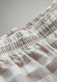 Brūns un balts kvadrāts audums ar savilktu elastīgu jostasvietu, parādot mīkstu tekstūru un austu rakstu.