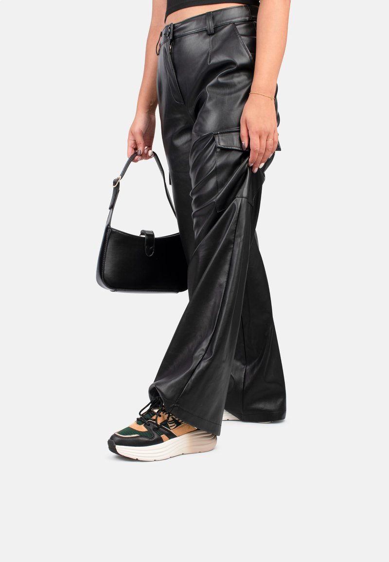 Pantalones de cuero sintético negros de pierna ancha con bolsillos tipo cargo y costuras decorativas. Combinados con un bolso negro y zapatillas gruesas multicolores.