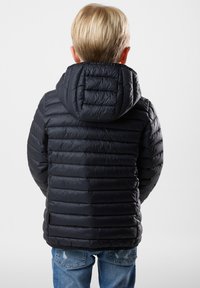 Sort dunjakke med vandrette syninger og hætte, der har en glat, skinnende tekstur. Bæres med lyseblå, slidte jeans.