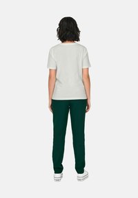 T-shirt en coton blanc à manches courtes, associé à un pantalon vert foncé et des baskets blanches, vu de dos sur un fond uni.