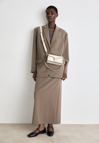 Brun skräddarsydd kavaj med axelspännen, matchande brun pennkjol, grå tröja och svarta ballerinas. Accessoarer inkluderar en krämfärgad crossbody-väska.