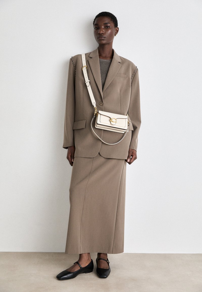 Brun skräddarsydd kavaj med axelspännen, matchande brun pennkjol, grå tröja och svarta ballerinas. Accessoarer inkluderar en krämfärgad crossbody-väska.
