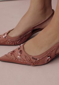 Vaaleanpunaiset mokkaisten korkokenkien slingback-mallit, joissa on teräväkärkinen muotoilu, ja joita koristavat kukkasekvenssikuvioinnit sekä helmikoristeet sivuilla.