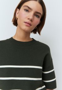 Pulover verde tricotat cu mâneci scurte, având dungi orizontale albe și un guler rotund cu textură ribată. Textură moale și croială lejeră.