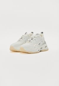 Fehér, sportos sneaker, amely vastag dizájnnal rendelkezik, texturált nylonnal és bőrrel, gumitalppal, valamint középső fűzéssel és márkázott díszítésekkel.